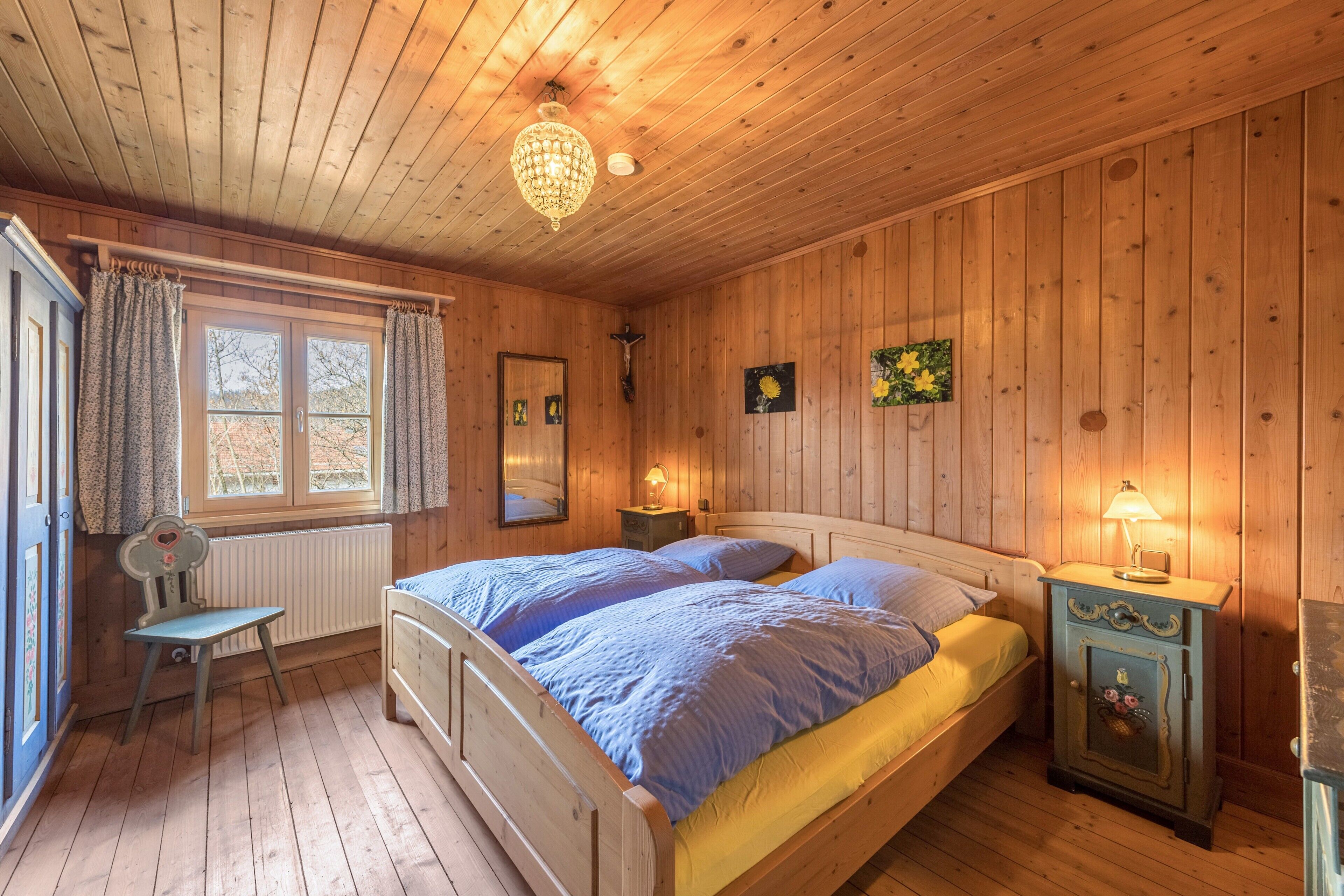 A wooden-paneled room with a bed, a chair, a nightstand, and a radiator.