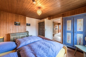 Une pièce aux murs lambrissés, comprenant un lit, une commode et une porte donnant sur une autre pièce.