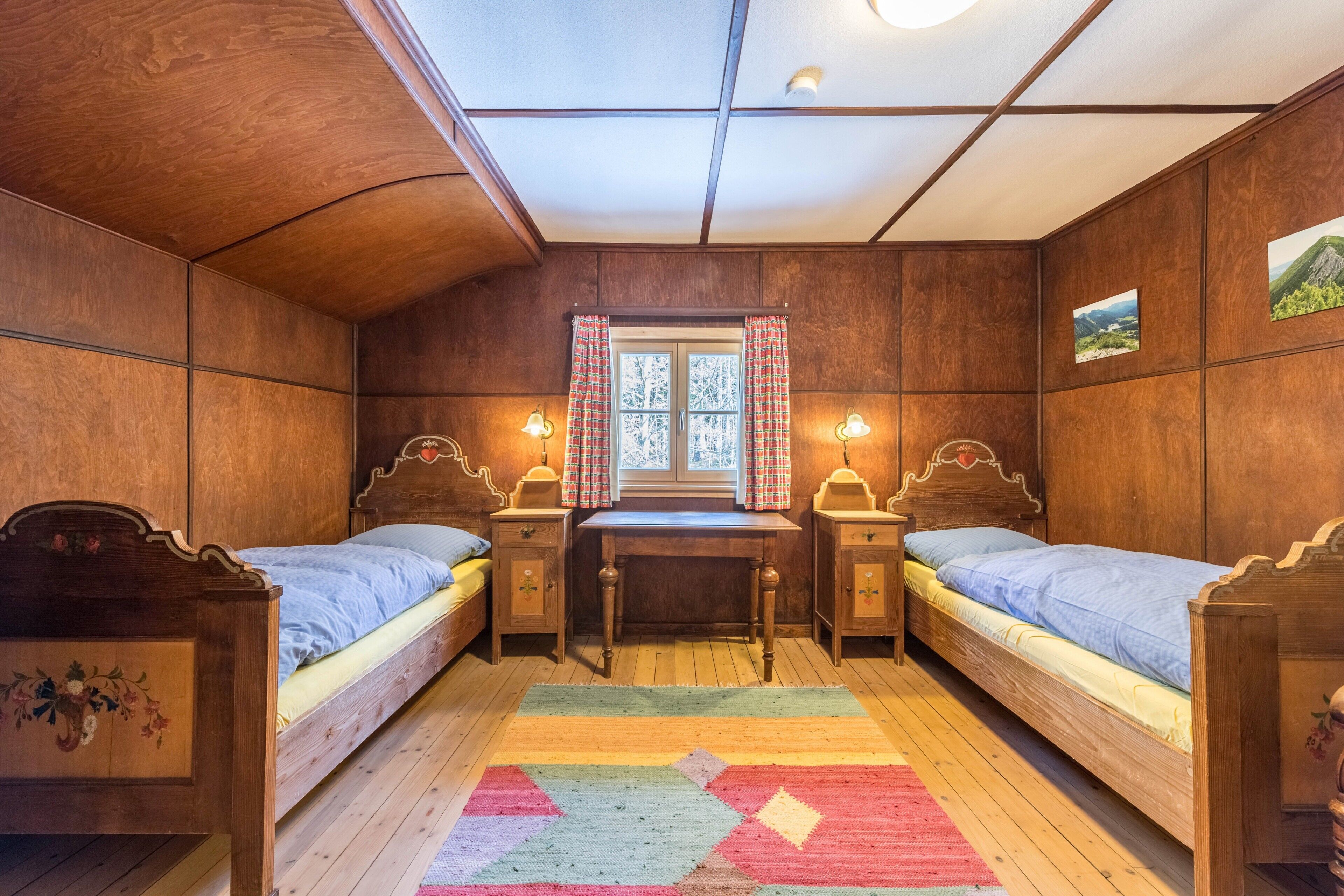 Ein Zimmer mit Holzboden, zwei Betten, einem Schreibtisch und einem Fenster mit Vorhängen.