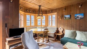 Ein Holzblockhaus-Innenraum mit Esstisch, Stühlen, einer Couch, einem Fernseher und Wanddekorationen.