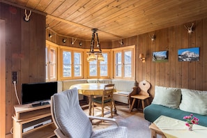 A wooden cabin interior with a dining table, chairs, a sofa, a television, and wall-mounted decor.