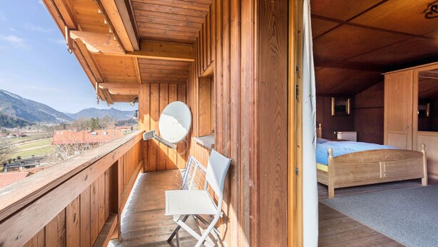 Ein hölzerner Balkon mit Stuhl, Bett und Bergblick.