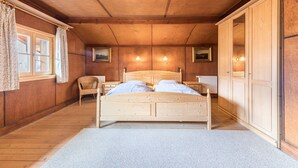 Ein Zimmer mit Holzwänden, einem Bett, einem Sessel und einem Kleiderschrank.