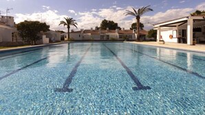 Une piscine aux eaux cristallines, délimitée par des couloirs, entourée de bâtiments blancs et de palmiers.