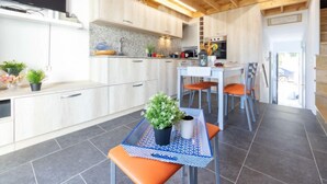 Une cuisine moderne avec des meubles en bois, un coin repas comprenant une table et des chaises, et un téléviseur fixé au mur.