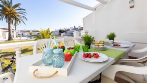 Une terrasse avec une table dressée pour un repas, agrémentée d’un plateau de fruits, d’une assiette de baies et d ’une petite plante en pot.