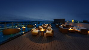 A rooftop lounge with outdoor seating and tables, overlooking a cityscape at dusk. - THIRD Ishigaki (Ishigaki)
