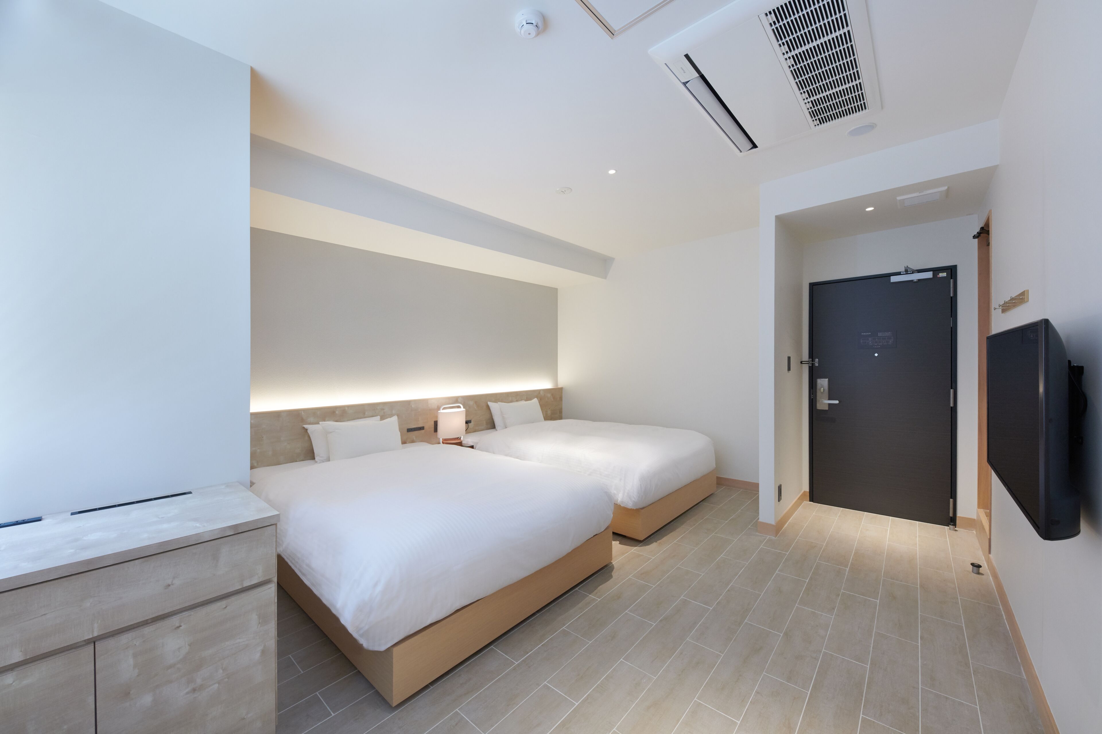 Una habitación de hotel moderna con dos camas, un televisor de pantalla plana y una mesita de noche de madera.