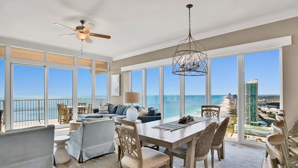 Ein geräumiger Balkon mit Blick auf Strand und Meer, ausgestattet mit einer Couch, Stühlen und einem Esstisch.