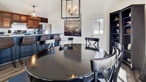 A modern kitchen with dark wood cabinets, a central island with bar stools, a dining table with chairs, and a pendant light above. - Luxe Private Truckee Getaway 20 Mins To Lake Tahoe (Truckee)