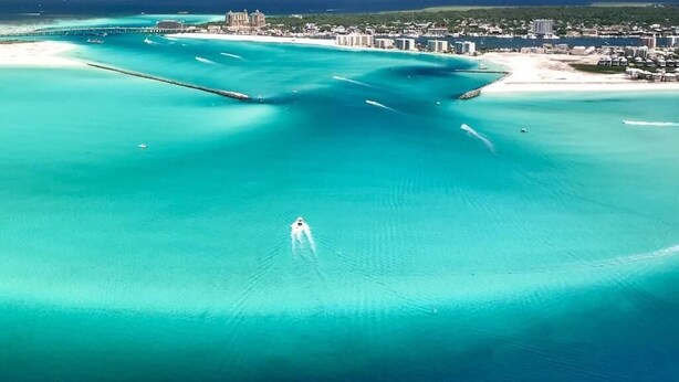 An aerial view of a coastal area with clear turquoise waters, a pier, and a resort with buildings along the shore. - Oasis on the Isle - Destin (Destin)