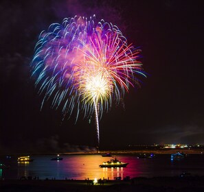 A nighttime view of a fireworks display over a body of water with boats and a docked ship. - Oasis on the Isle - Destin (Destin)
