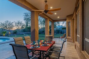 Une terrasse couverte avec une table dressée pour les repas, un ventilateur de plafond et une vue sur le jardin arrière.
