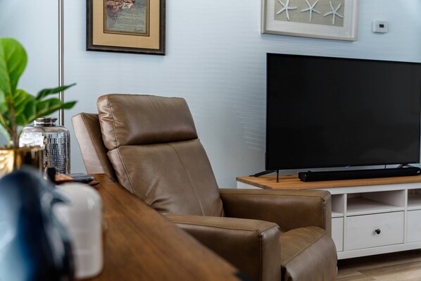 Un salon avec un canapé en cuir, un téléviseur à écran plat posé sur un meuble en bois et un certificat encadré accroché au mur.