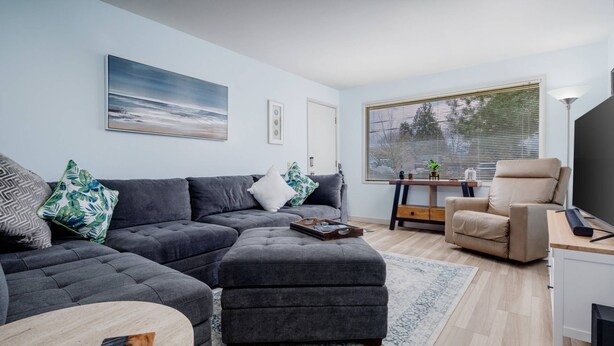 A modern living room with a grey sectional sofa, a beige armchair, a coffee table, and a large window with blinds. - Bright and Delightful Renovation, Single Level, Fenced Backyard, 3 Blocks to MAX, 25 Min to Portland (Hillsboro)