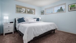 A bedroom with a bed, a nightstand, a lamp, and two windows with blinds. - Bright and Delightful Renovation, Single Level, Fenced Backyard, 3 Blocks to MAX, 25 Min to Portland (Hillsboro)
