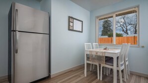 A compact kitchen with a stainless steel refrigerator, a dining table with four chairs, and a window with blinds. - Bright and Delightful Renovation, Single Level, Fenced Backyard, 3 Blocks to MAX, 25 Min to Portland (Hillsboro)