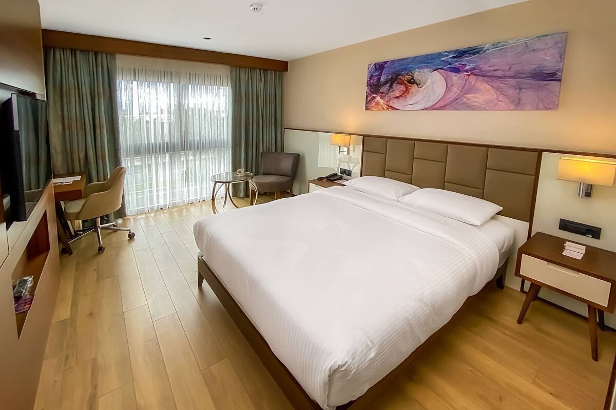Habitación de hotel con una cama grande, un escritorio, una silla, una mesita y un cuadro en la pared.