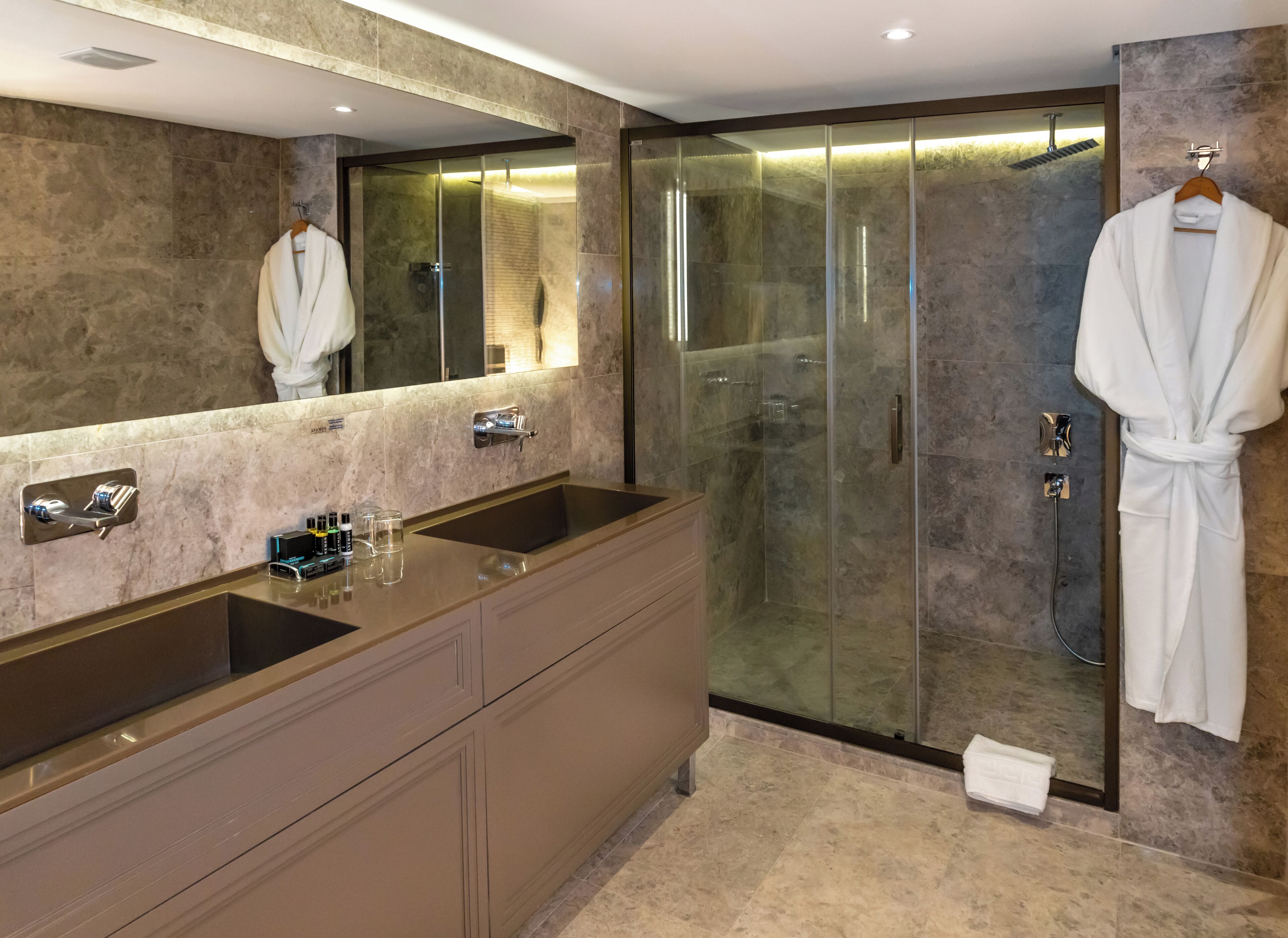 A modern bathroom with two sinks, a glass-enclosed shower, and a robe hanging on a hook.