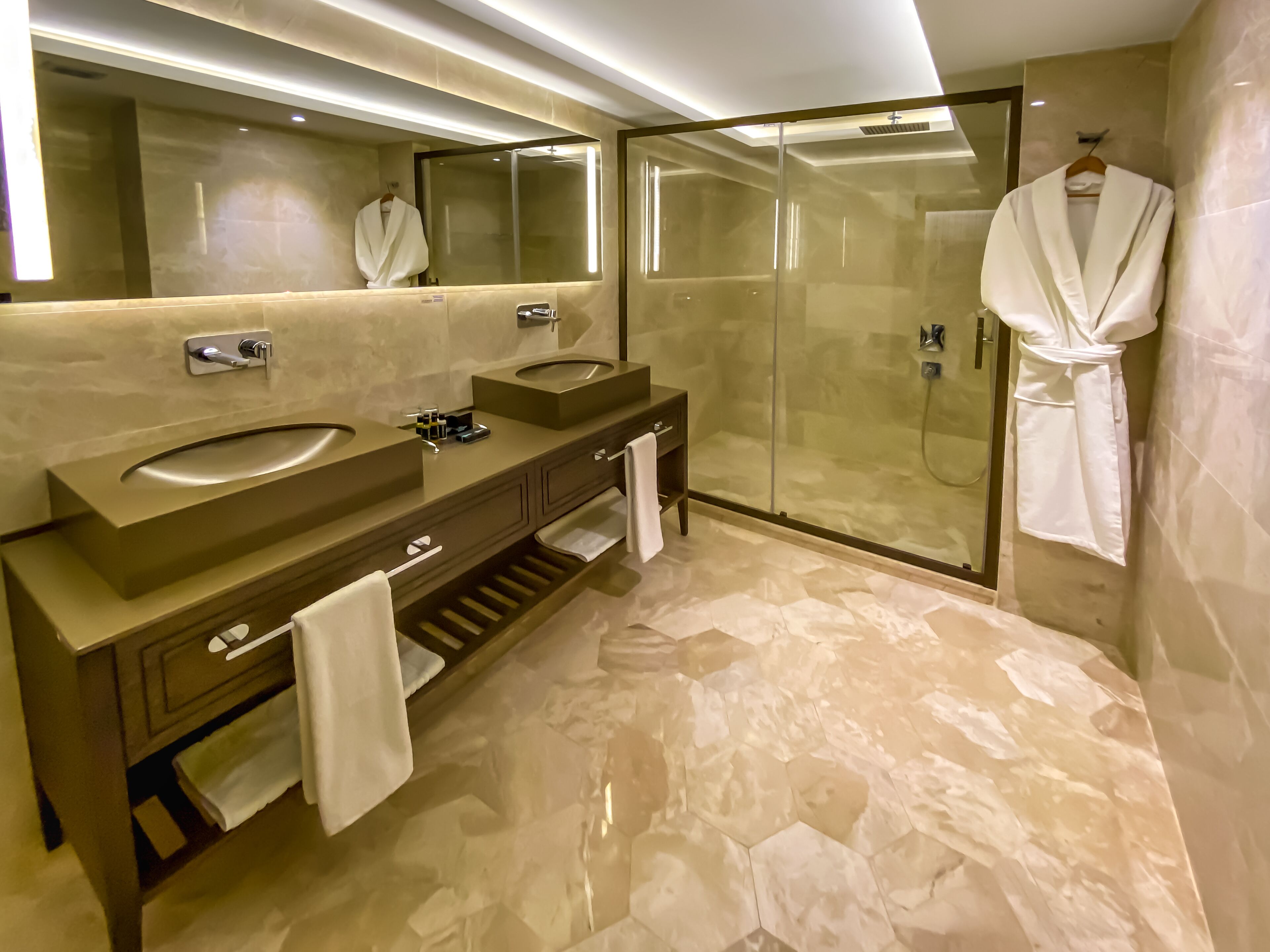 A modern bathroom with two sinks, a glass shower enclosure, and a robe hanging on the wall.