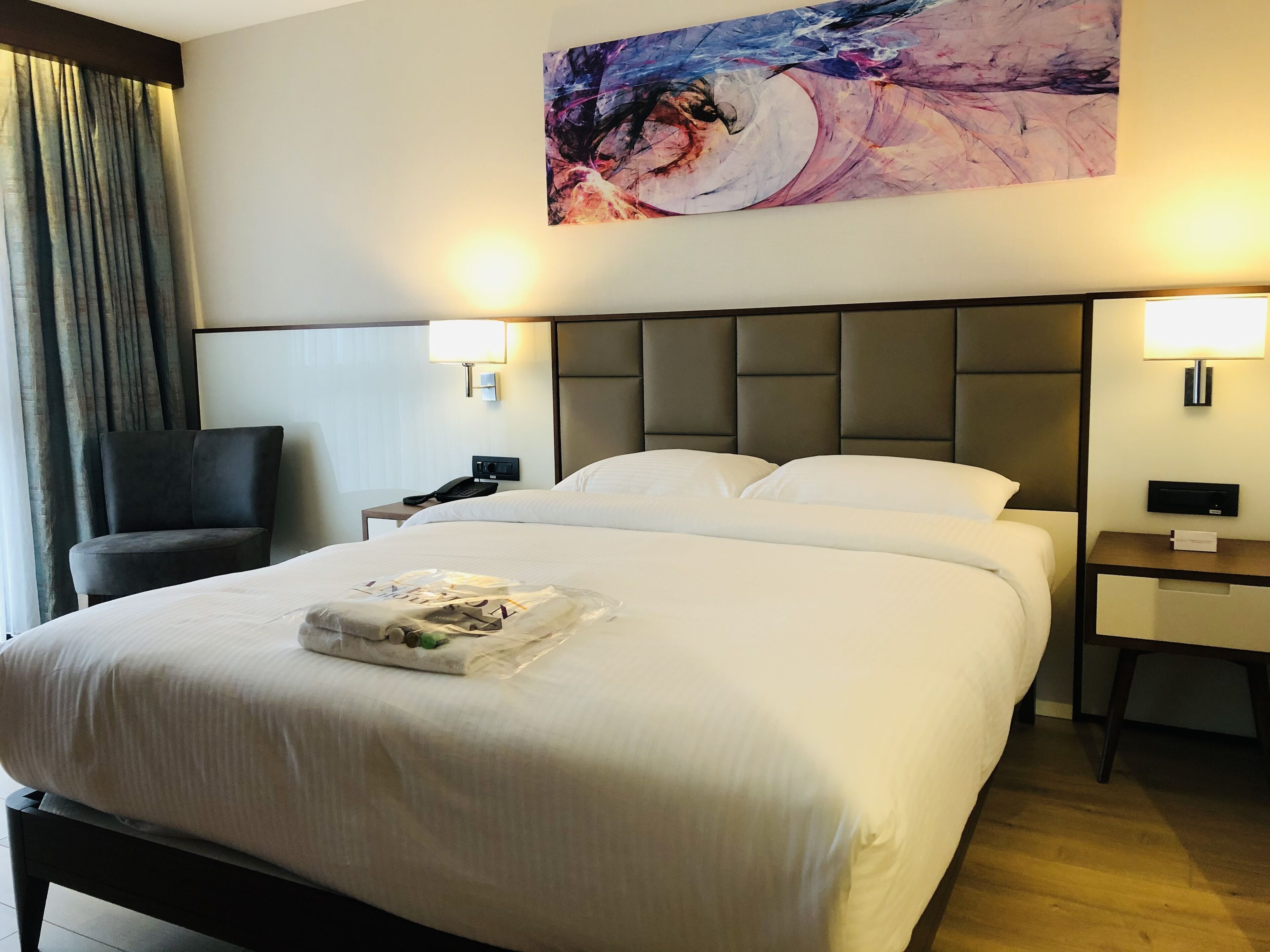Habitación de hotel con una cama grande, una silla, una mesita de noche con un teléfono y un cuadro en la pared.