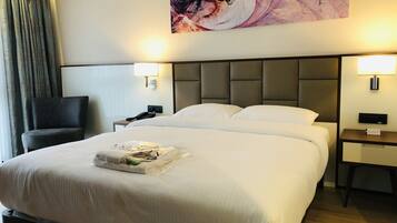 Habitación de hotel con una cama grande, una silla, una mesita de noche con un teléfono y un cuadro en la pared.