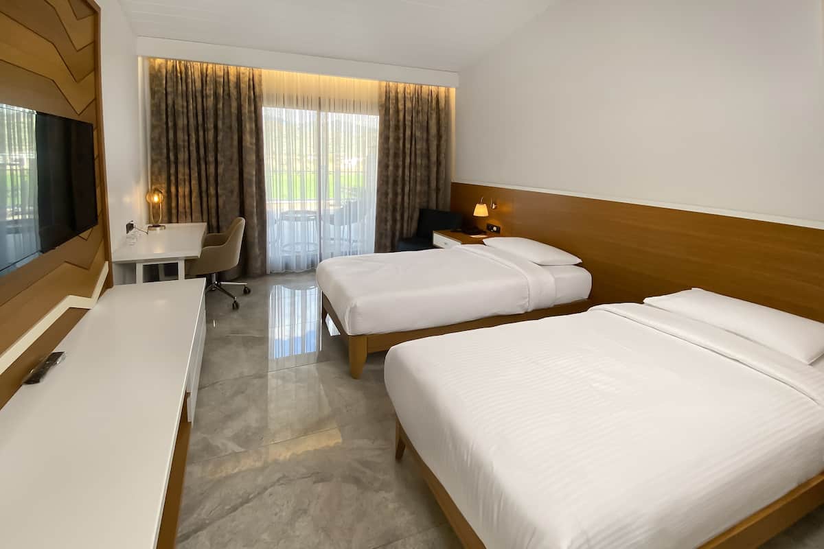 Habitación de hotel con dos camas, un escritorio, una silla, un televisor y una ventana con cortinas.