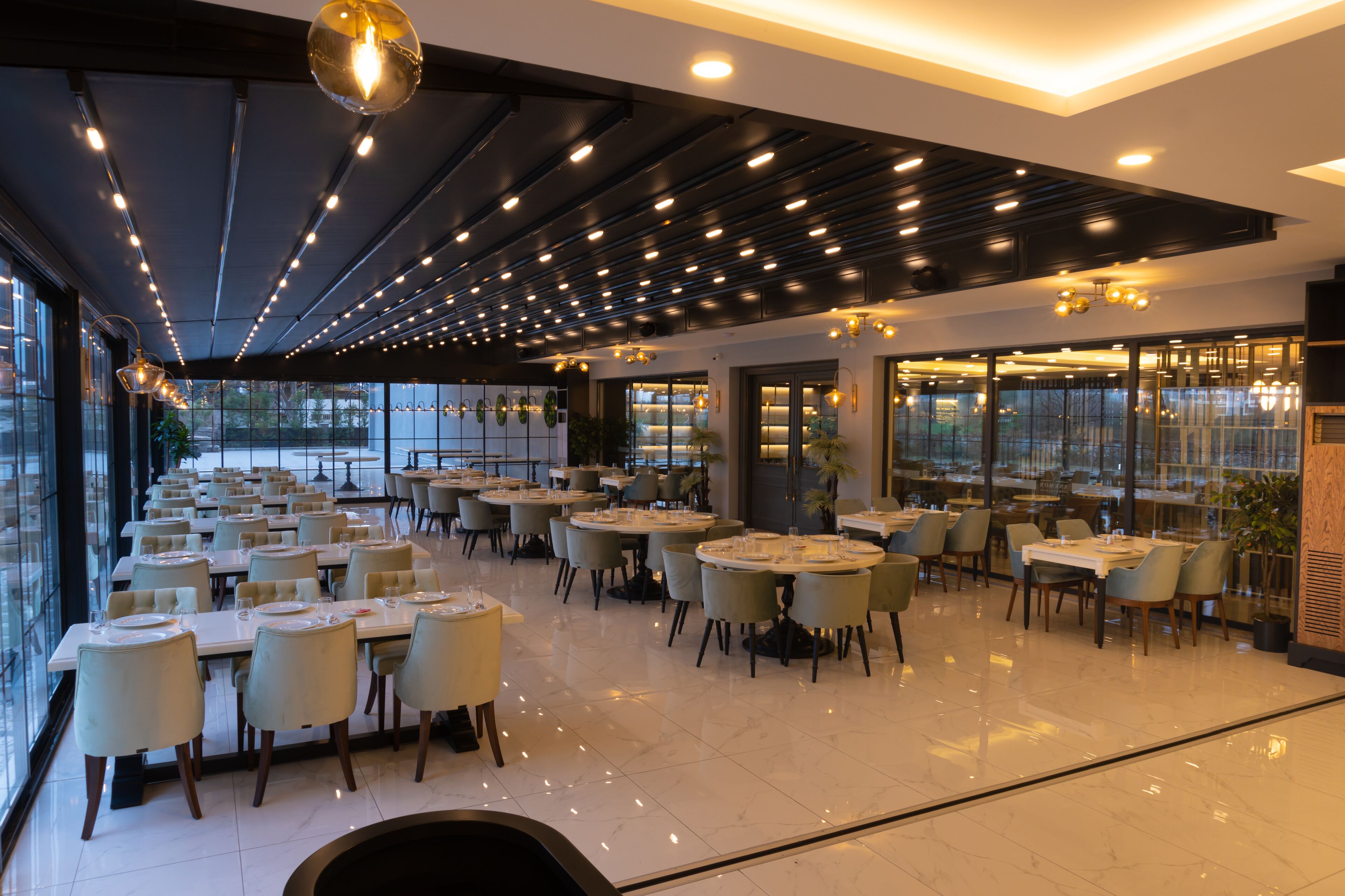 Un restaurant spacieux, doté de nombreuses tables et chaises, de grandes fenêtres et d’un design moderne au niveau du plafond.