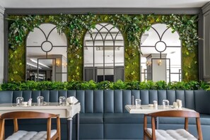 Un restaurant doté d’un mur végétal, de sièges bleus et de tables blanches.
