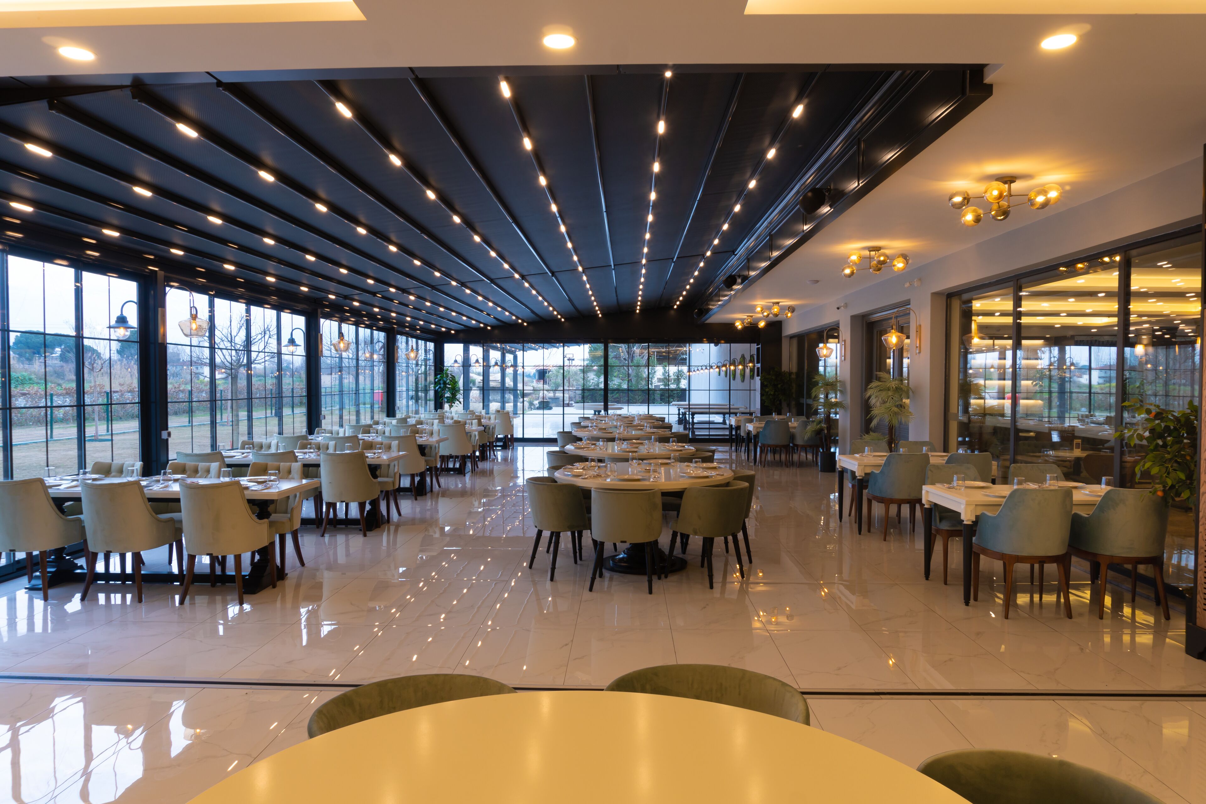 Un espace de restauration moderne doté de nombreuses tables et chaises, de grandes fenêtres et d’un plafond agrémenté de luminaires linéaires.