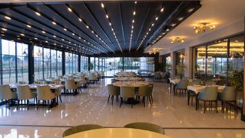 Un espace de restauration moderne doté de nombreuses tables et chaises, de grandes fenêtres et d’un plafond agrémenté de luminaires linéaires.