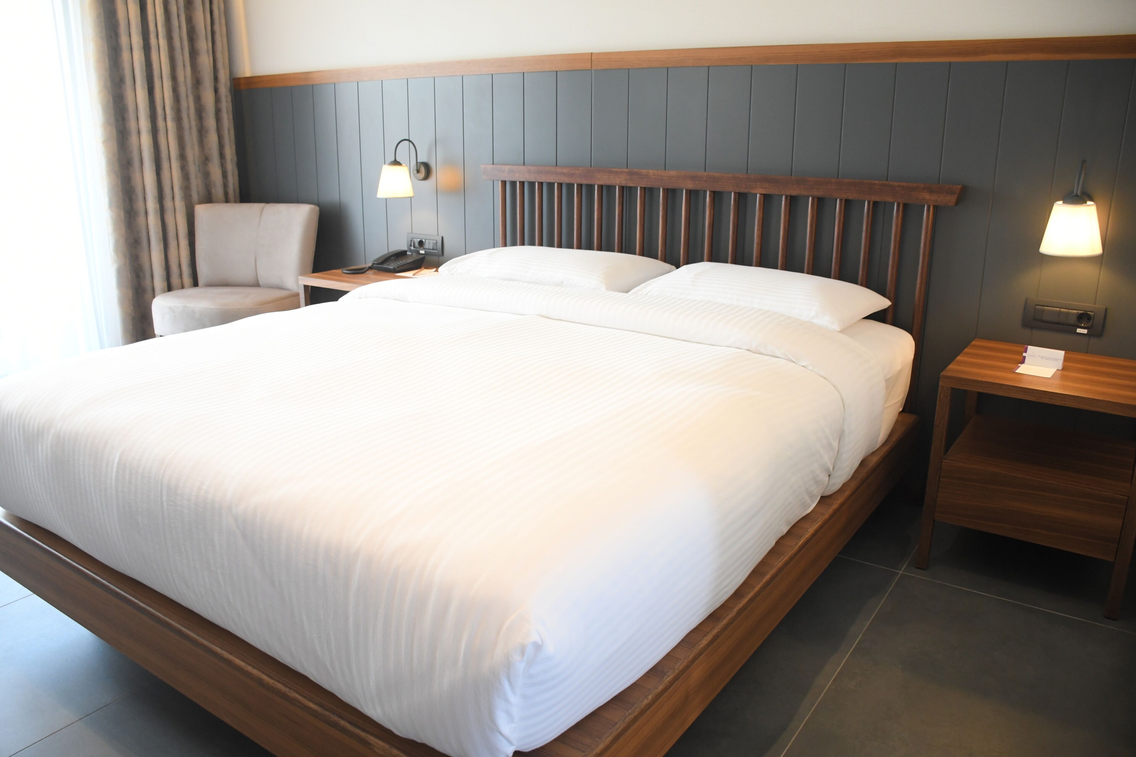 Une chambre d’hôtel avec un grand lit, deux tables de chevet, une chaise et une lampe.
