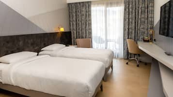 Quarto de hotel com duas camas, uma escrivaninha, uma cadeira, televisão e janela com cortinas.