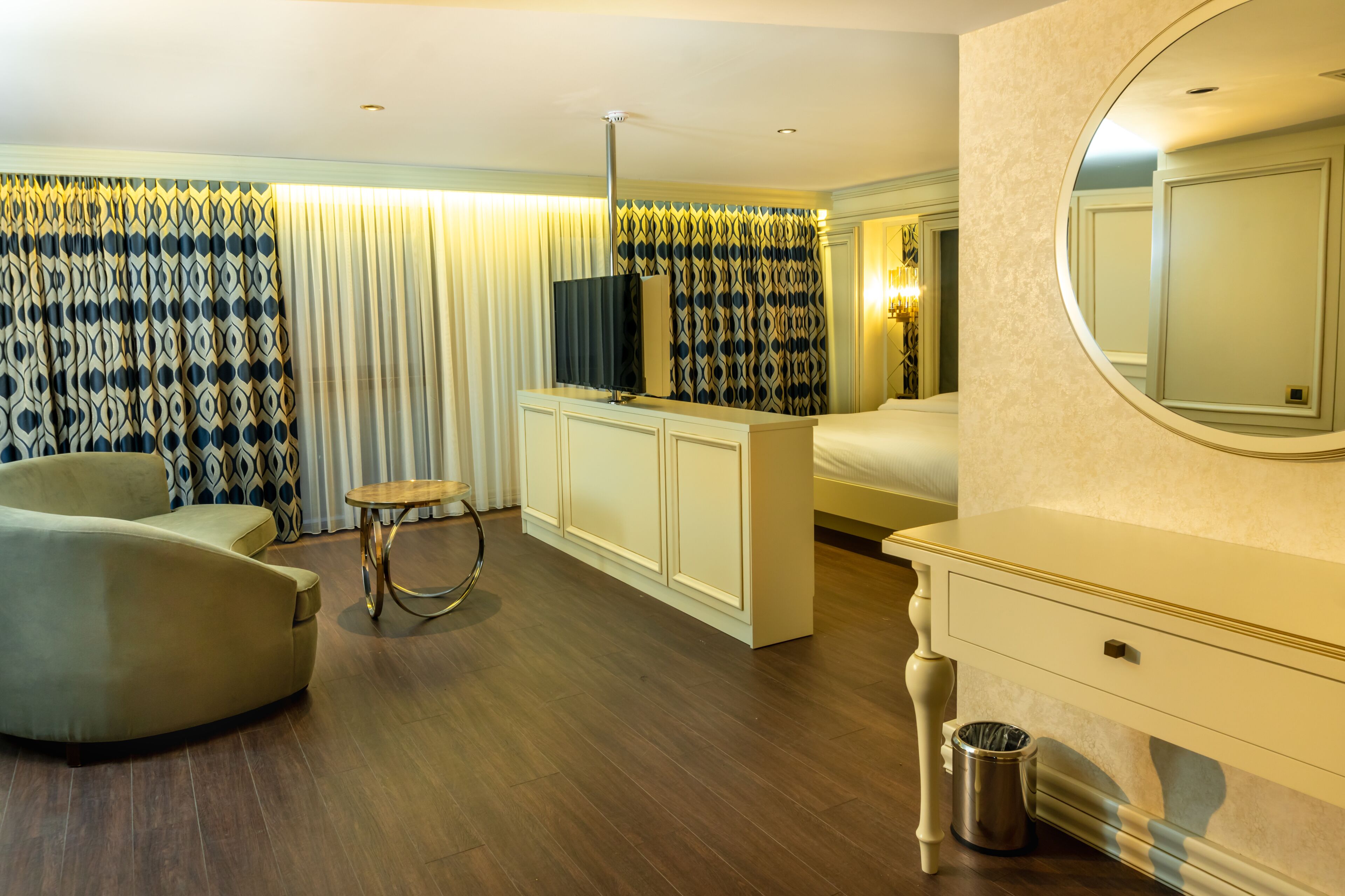 A hotel room with a sofa, a small round table, a TV, a bed, a dresser, and a mirror.