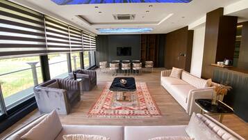 A modern living room with a large window, a ceiling projection of a night sky, and a seating area with sofas and a coffee table.