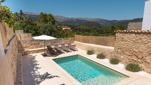 Una piscina rettangolare con acqua cristallina, circondata da un muro in pietra e affacciata su montagne sullo sfondo.