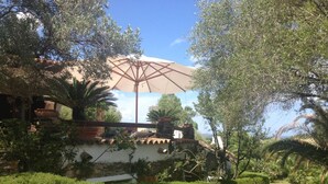 Een tuin met terras, een stenen muur en een grote parasol.
