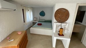 Een kleine slaapkamer met een bed, nachtkastje, kaptafel en een decoratief wandobject.