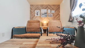 A cozy room with two wicker chairs, a wooden table, and a wall decorated with framed pictures. - Rusutsu Grand Cabin (Kimobetsu)