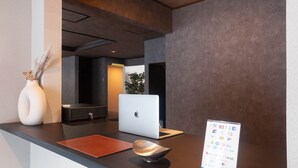A reception desk with a laptop, a vase with dried flowers, a brochure stand, and a dark wall. - Rusutsu Grand Cabin (Kimobetsu)