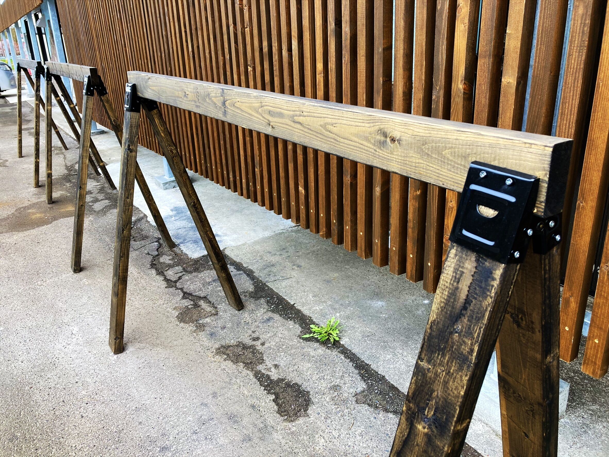 A wooden bench with a metal bracket attached to a wooden post, set against a vertical wooden slat wall.