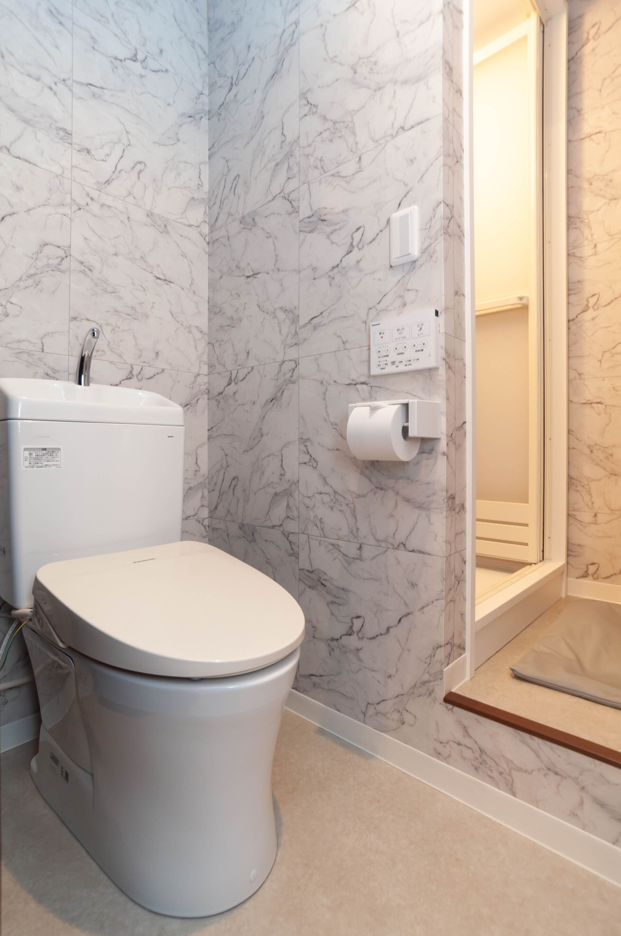 A bathroom with a toilet, marble walls, a shower, and a toilet paper holder.