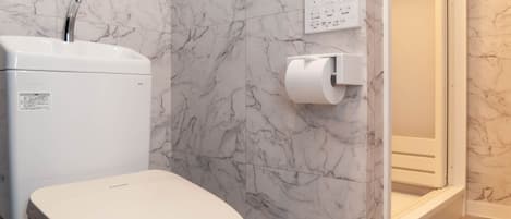 A bathroom with a toilet, marble walls, a shower, and a toilet paper holder.