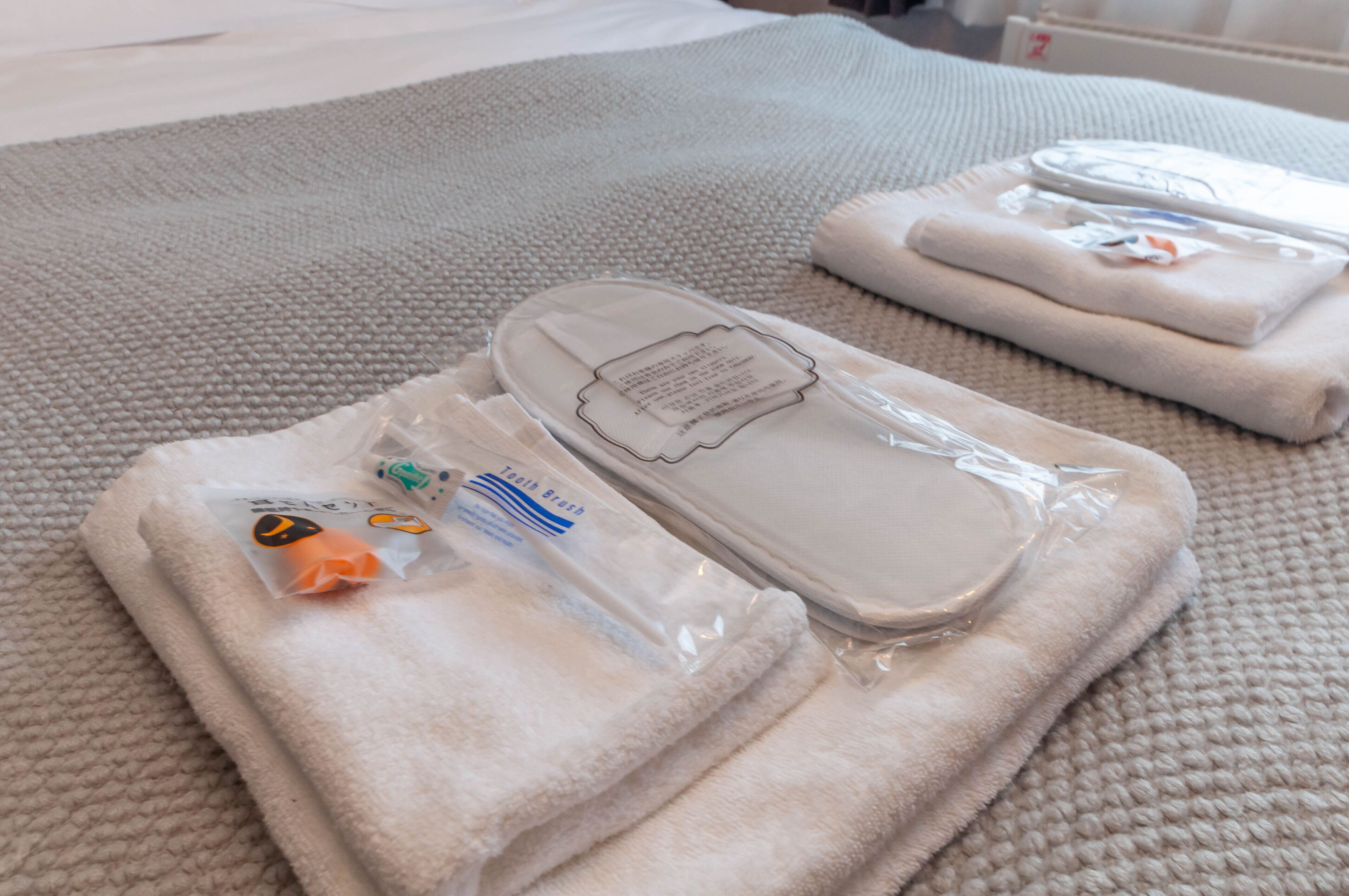 Neatly folded towels and slippers on a textured bedspread.
