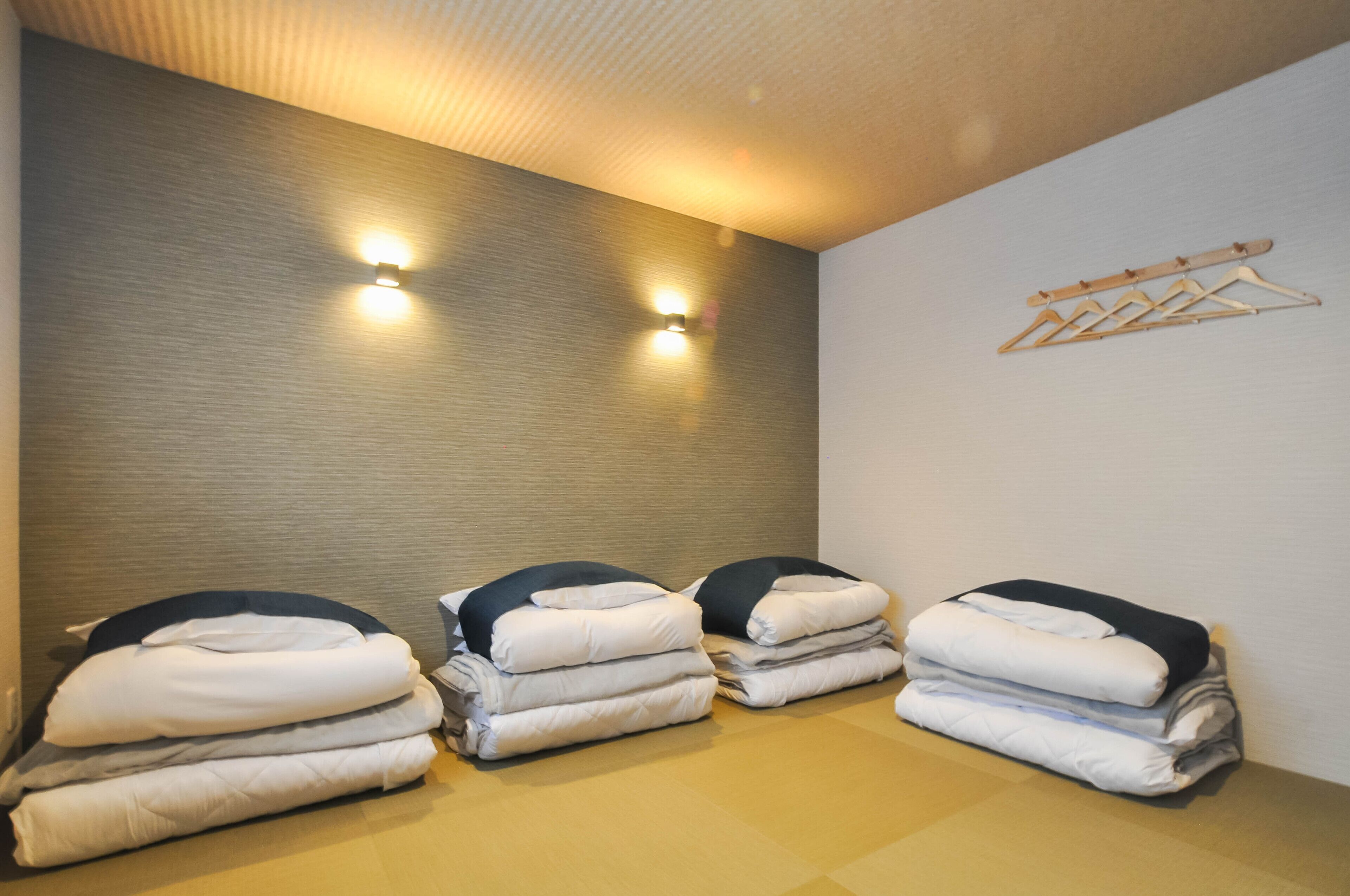 A room with a textured wall, two wall-mounted lights, a wooden hanger rack, and neatly stacked folded blankets.