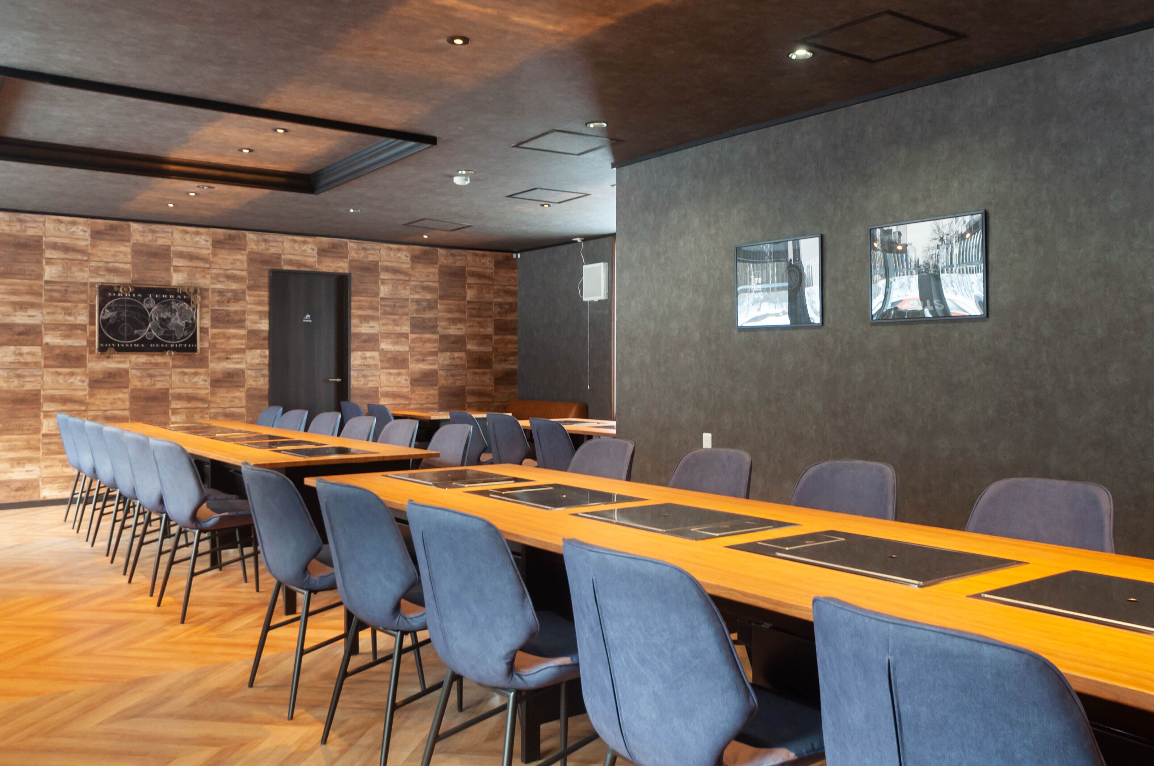 Ein Konferenzraum mit einem langen Tisch, blauen Stühlen und zwei gerahmten Bildern an der Wand.