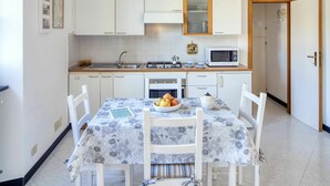 Cocina funcional con armarios blancos, microondas, estufa y lavabo. Hay una mesa de comedor con sillas y un bol de fruta.