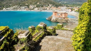 Un pueblo costero con edificios a lo largo de la orilla, un mar azul cristalino y montañas al fondo.