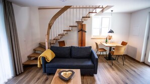 A modern living room with a dark blue sofa, wooden staircase, and a dining area with a table and chairs. - Douglasie - Siegelsbacher Mühle (Siegelsbach)