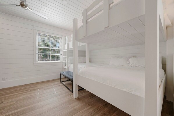 A bunk bed room with white walls, a window with blinds, and a wooden floor.